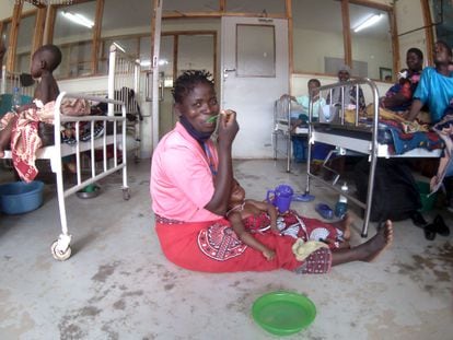 Una mujer sostiene en los brazos a su hijo mientras almuerza en el suelo de una sala de pediatría del hospital de Kamuzu, en Malawi.