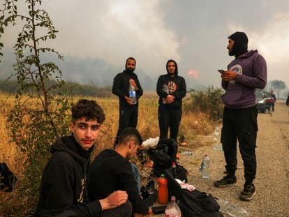 Un grupo de migrantes encontrado por los bomberos griegos permanece al lado de una carretera, mientras sigue activo el incendio en el parque nacional de Dadiá, en la región de Evros (Grecia), este viernes.