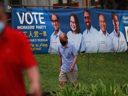 Varias personas pasean ante un cartel del Partido de los Trabajadores, en la oposición, en vísperas de las elecciones generales de Singapur, este viernes.