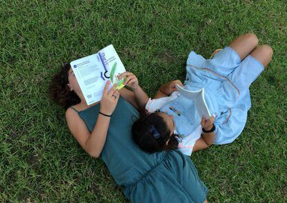 Dos ni&ntilde;as leyendo, o simulando que leen, en un parque.