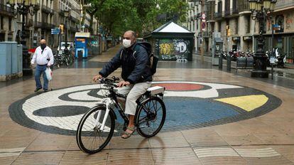 Un hombre protegido con mascarilla pasea en bicicleta por las Ramblas de Barcelona, prácticamente vacías en el quincuagésimo séptimo día del estado de alarma.