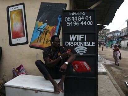 Un ciudadano navega por internet desde su móvil junto a un locutorio en una calle de Abiyán, Costa de Marfil.