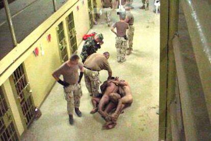 Militares estadounidenses ante presos iraquíes, desnudos y esposados unos a otros, en Abu Ghraib.