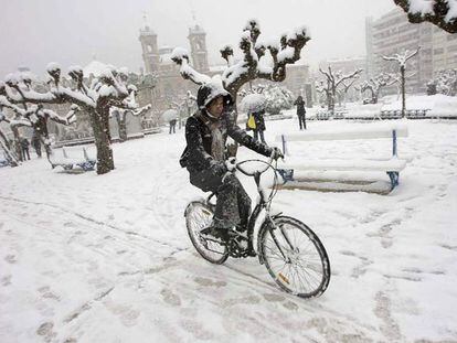 Una ciclista desafía a la nieve en los jardines de Alderdi Eder, con el Ayuntamiento donostiarra al fondo.
