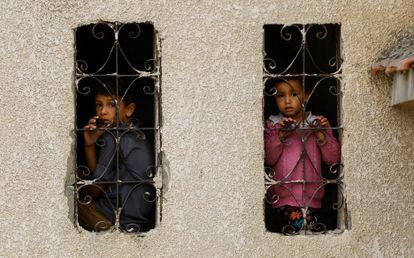 Niños palestinos miran a través de las ventanas mientras ocurren ataques israelíes a casas, este jueves en Jan Yunis.