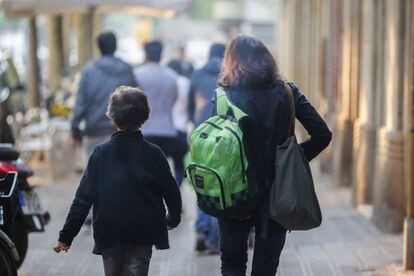 Una madre lleva la mochila de su hijo camino del colegio.