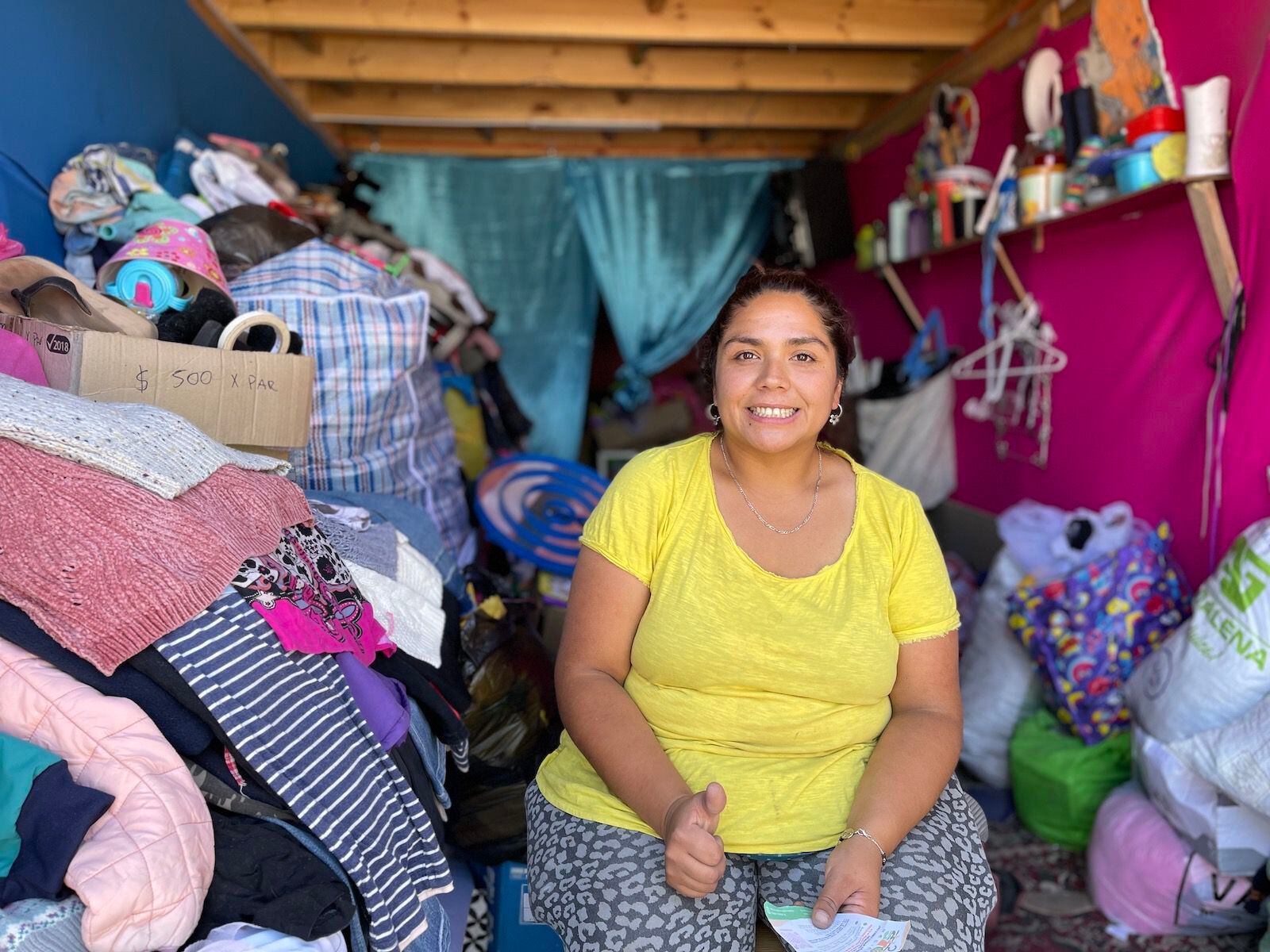 Jazmín Yañez posa junto a un montón de ropa de segunda mano que venderá en la tienda Stop Recicla.