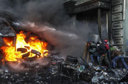 Activistas proeuropeos se cobijan de los chorros de agua que lanzaban las fuerzas gubernamentales durante los disturbios que vivía Kiev, la capital de Ucrania. Una pila de neumáticos ardía mientras tanto.