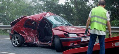 Un coche accidentado en una carretera de Asturias es recogido por una gr&uacute;a.