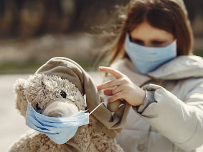 Una niña con mascarilla juega con su oso de peluche