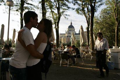 Dos jóvenes se besan en una terraza entre el paseo del Prado y la plaza de Oriente, detrás la catedral de La Almudena de Madrid.