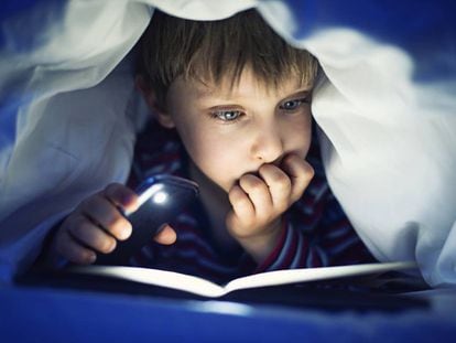 Un niño leyendo un libro iluminado por la luz del móvil