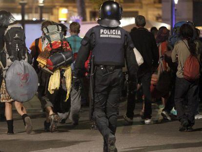 Varios acampados abandonan la plaza de Catalunya bajo la mirada de un 'mosso'.