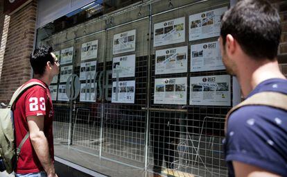 Dos personas observan el escaparate de una empresa inmobiliaria. 