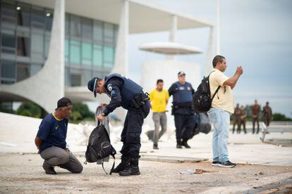 Luego de los disturbios, un policía examina la mochila de un hombre esposado.