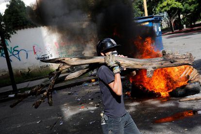Un opositor al gobierno venezolano carga una pieza de madera para construir una barricada.