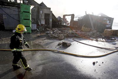 Un bombero pasa ante los restos de la conservera Lago Paganini, después de que un fuego la arrasase, en Cangas.