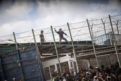 Un antidisturbio marroquí apunta con una pierda hacia los migrantes subsaharianos en la valla que separa el territorio marroquí y el español en Melilla.