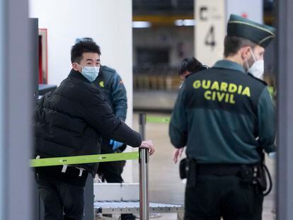 Un agente de la Guardia Civil con un pasajero que llega al aeropuerto Adolfo Suárez Madrid-Barajas procedente de un vuelo de Chongqing (China).