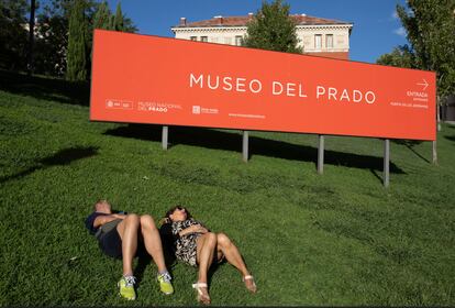 Dos personas tumbadas junto al cartel del Museo del Prado. 