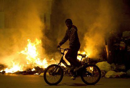 Un niño pasa en bicicleta ante uno de los incendios provocados. Los vecinos tratan de mantener una vida normal pese a que la situación en la ciudad andaluza es límite tras casi tres semanas de huelga de basuras.