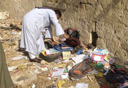 Un hombre revisa entre los libros y mochilas que fueron lanzados por el autobús accidentado esta mañana en Egipto.