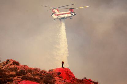 Un helicóptero deja caer agua cerca de un bombero parado en una ladera pintada con retardante de fuego mientras el incendio de Fairview arde cerca de Hemet, el 6 de septiembre de 2022.