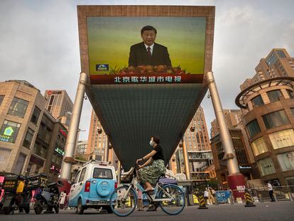 Una mujer pasea en bici bajo una pantalla en la que Xi Jinping pronuncia un discurso, en Pekín.