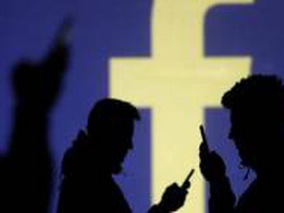 Varias personas consultan su móvil frente a un logo de Facebook.