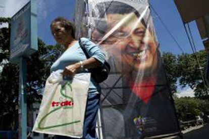 Una mujer camina frente a un poster de Hugo Chávez