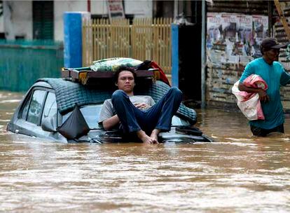 Un ciudadano indonesio descansa sobre el capó de un coche mientras otro camina a través de una calle inundada en Yakarta. Entre un 50% y un 70% de la capital continúa sumergida bajo el agua.