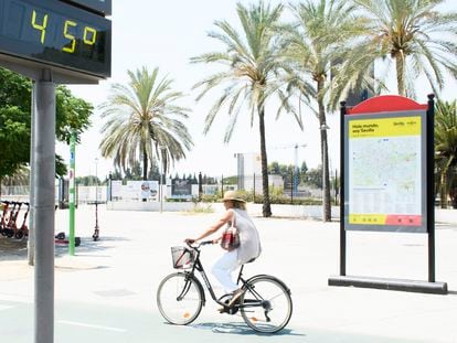 Una mujer en bicicleta pasa junto a un termómetro de calle en Sevilla que marca 45 grados, este viernes.