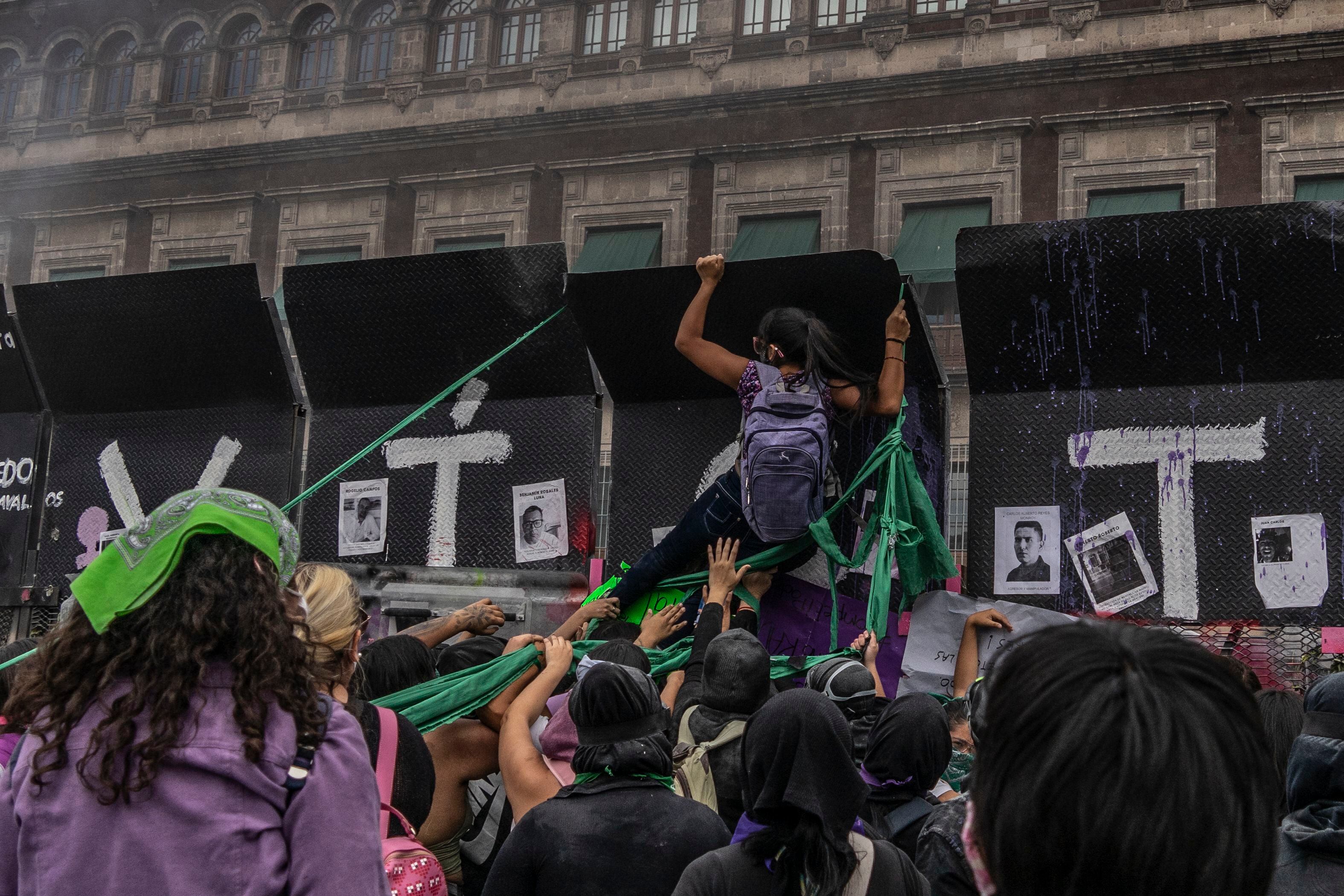 Una mujer se cuelga de una de las vallas instaladas afuera de Palacio Nacional durante la protesta del 8-M en Ciudad de México.