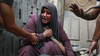 Una mujer palestina herida llora mientras sostiene la mano de su familiar muerto frente a su casa, tras los ataques aéreos israelíes dirigidos contra su barrio en la ciudad de Gaza, este lunes.