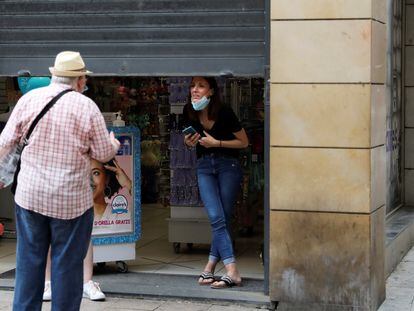 Un comerciante habla con una persona con la persiana medio bajada en Lleida.