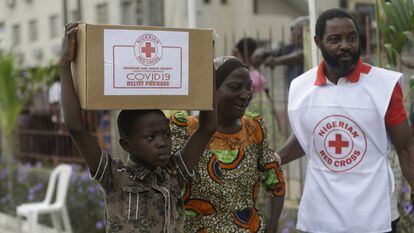 Un niño y su madre en el suburbio de Makoko, en Lagos, transportan una caja con comida que han recibido de la Cruz Roja nigeriana el pasado domingo.
