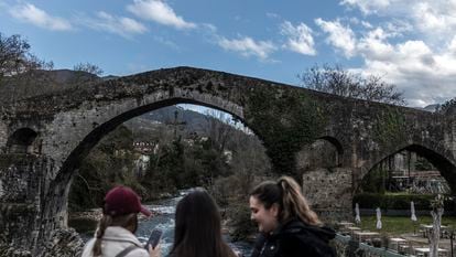 Tres jóvenes miran en sus teléfonos las fotos que se han hecho, en el puente romano de Cangas de Onís.