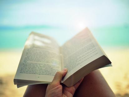 Una personas lee un libro en la playa.
