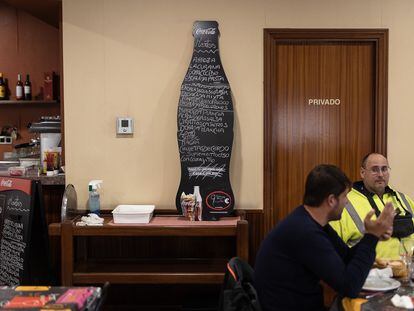 Dos clientes comen en la sala del restaurante Regino de Barcelona junto a un cartel que anuncia los platos y el precio del menú.