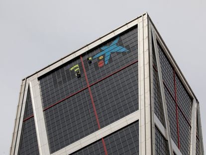 Varios operarios quitan el logotipo de Bankia para incorporar, sobre las ventanas más altas del edificio de Torre Europa de Madrid, la imagen de CaixaBank.