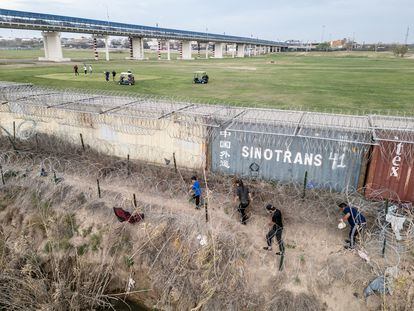 Migrants walk on the banks of the Rio Grande river to find a way to enter the U.S. as golfers play on the other side of the shipping container fence in Eagle Pass, Texas, U.S., February 27, 2024.