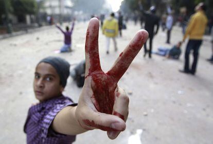 Un manifestante hace la señal de la victoria mientras otros arrojan piedras a la policía militar, cerca de la plaza de Tahrir, en El Cairo.
