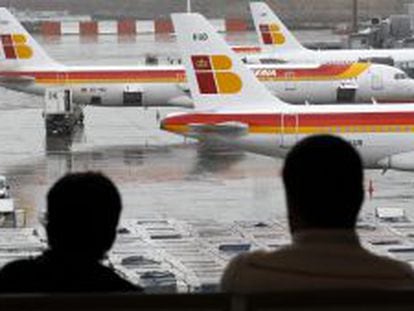 Dos pasajeros observan varios  aviones de la compa&ntilde;ia Iberia en las pistas de Barajas.