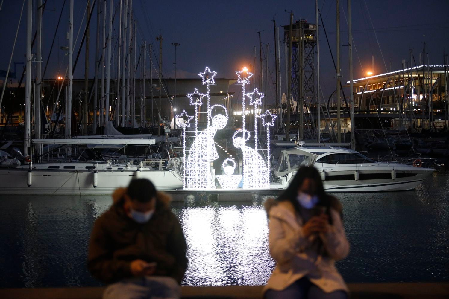 Dos personas junto a un Belén luminoso el día de la inauguración del encendido de luces de la segunda edición de 'Nadal al Port', en el puerto de Barcelona, el 2 de diciembre.
