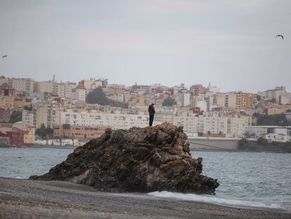 Un joven subido a una roca en la playa del Tarajal, el 22 de marzo;  al fondo, la ciudad de Ceuta.