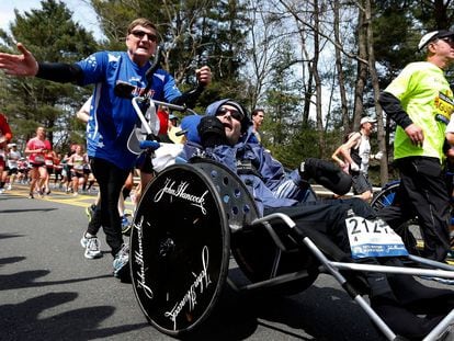 Rick Hoyt, center, is pushed by his father Dick, left, along the Boston Marathon course, April 15, 2013, in Wellesley, Mass. Hoyt, who with his father pushing his wheelchair became a fixture at the Boston Marathon and other races for decades, has died. He was 61. Hoyt died of complications with his respiratory system, his family announced on Monday, May 22, 2023. (AP Photo/Michael Dwyer, File)