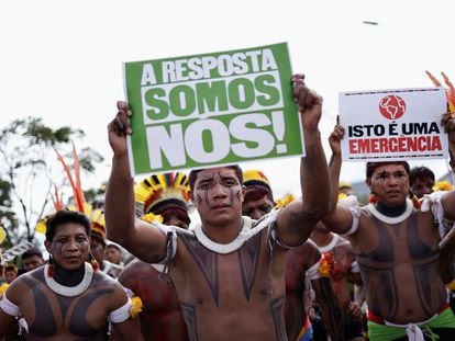 Dos indígenas brasileños levantan carteles con las frases "¡La respuesta somos nosotros!" y "Esto es una emergencia", durante una manifestación en Brasilia, el 24 de abril de 2024.