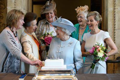 La princesa Ana (a la izquierda de la reina) y la condesa Sophie de  Wessex (con flores, a su derecha) acompañan a Isabel II mientras esta corta una tarta para celebrar los 100 años de un instituto federal de mujeres, en junio de 2015 en el Royal Albert Hall de Londres.
