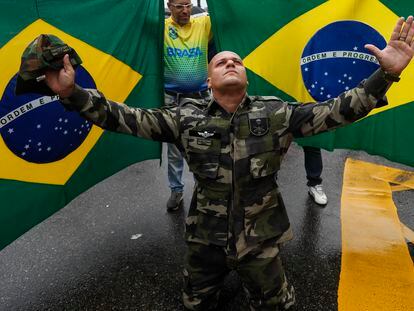 Jair Bolsonaro supporter wearing military clothes, kneeling in front of two Brazilian flags during Rio De Janeiro protests