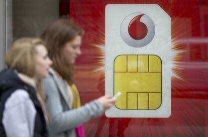 Una mujer consulta su m&oacute;vil ante un cartel de Vodafone en Londres.